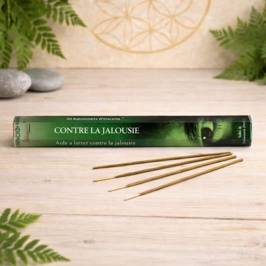 Coffret vert Encens Contre La Jalousie de Pierres énergétiques avec quatre bâtonnets d'encens sur une surface en bois clair, entourés de feuilles et de pierres naturelles pour une touche de bien-être.